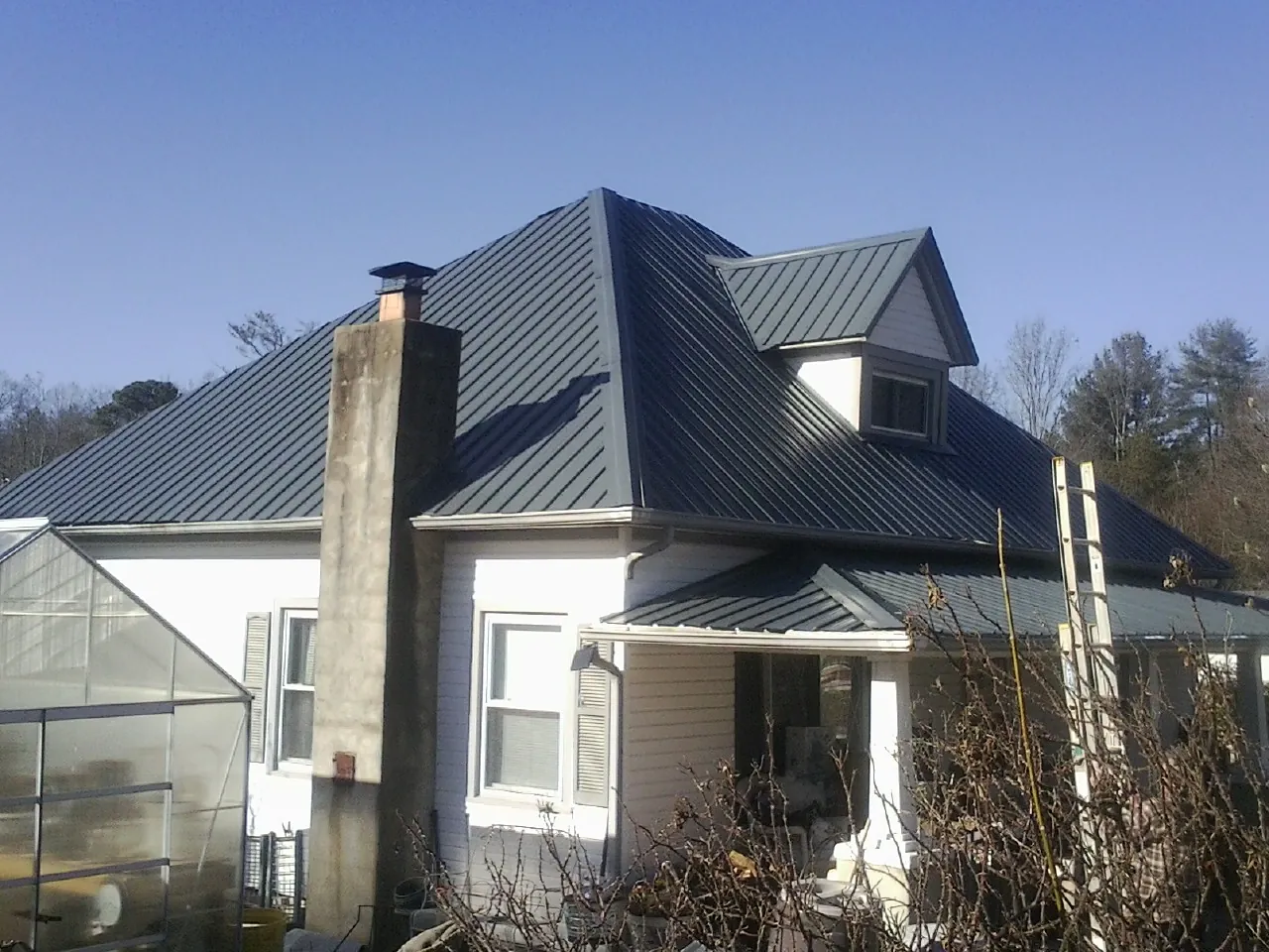 Dark blue standing seam metal roof on a white farmhouse with dormer — Slate & Tile Roof Repair by Roofing Brothers in Beatrice