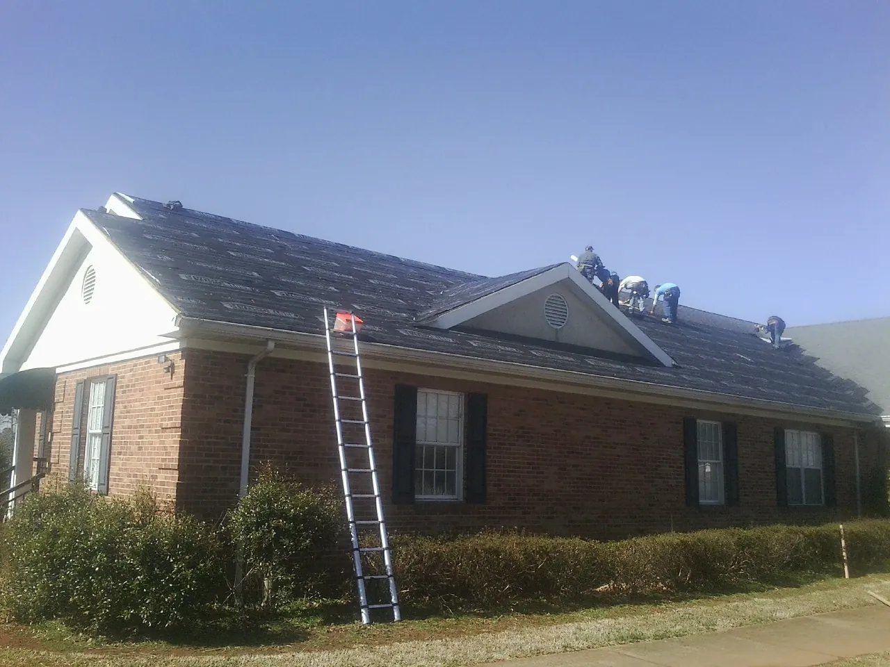 Crew tearing shingles off a brick ranch roof with a ladder set — Emergency Roof Repair work by our crew in Beatrice