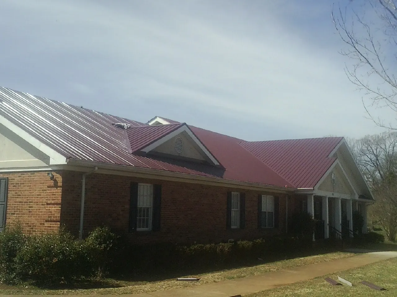 Red metal roof with gabled entries on a long brick building, from a Hail Damage Roof Repair job in Beatrice