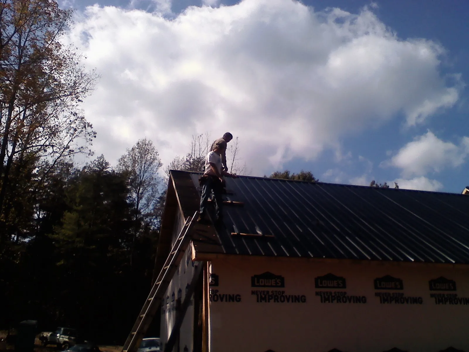 Roofer fastening dark metal panels high against a cloudy sky, from a Roof Inspection job in Beatrice