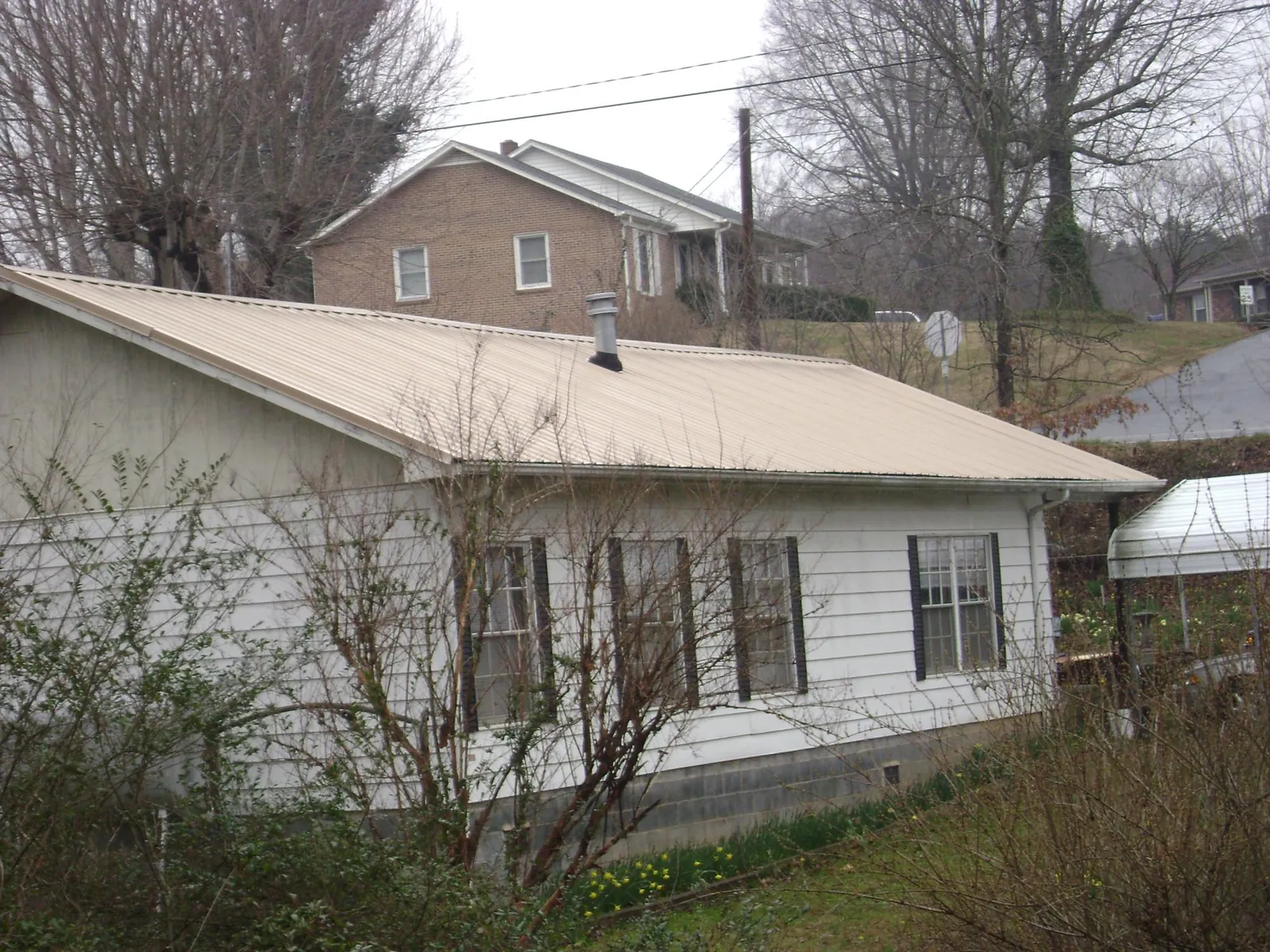 Tan metal roof on a white sided house set into a hillside — Commercial Roofing by Roofing Brothers in Beatrice