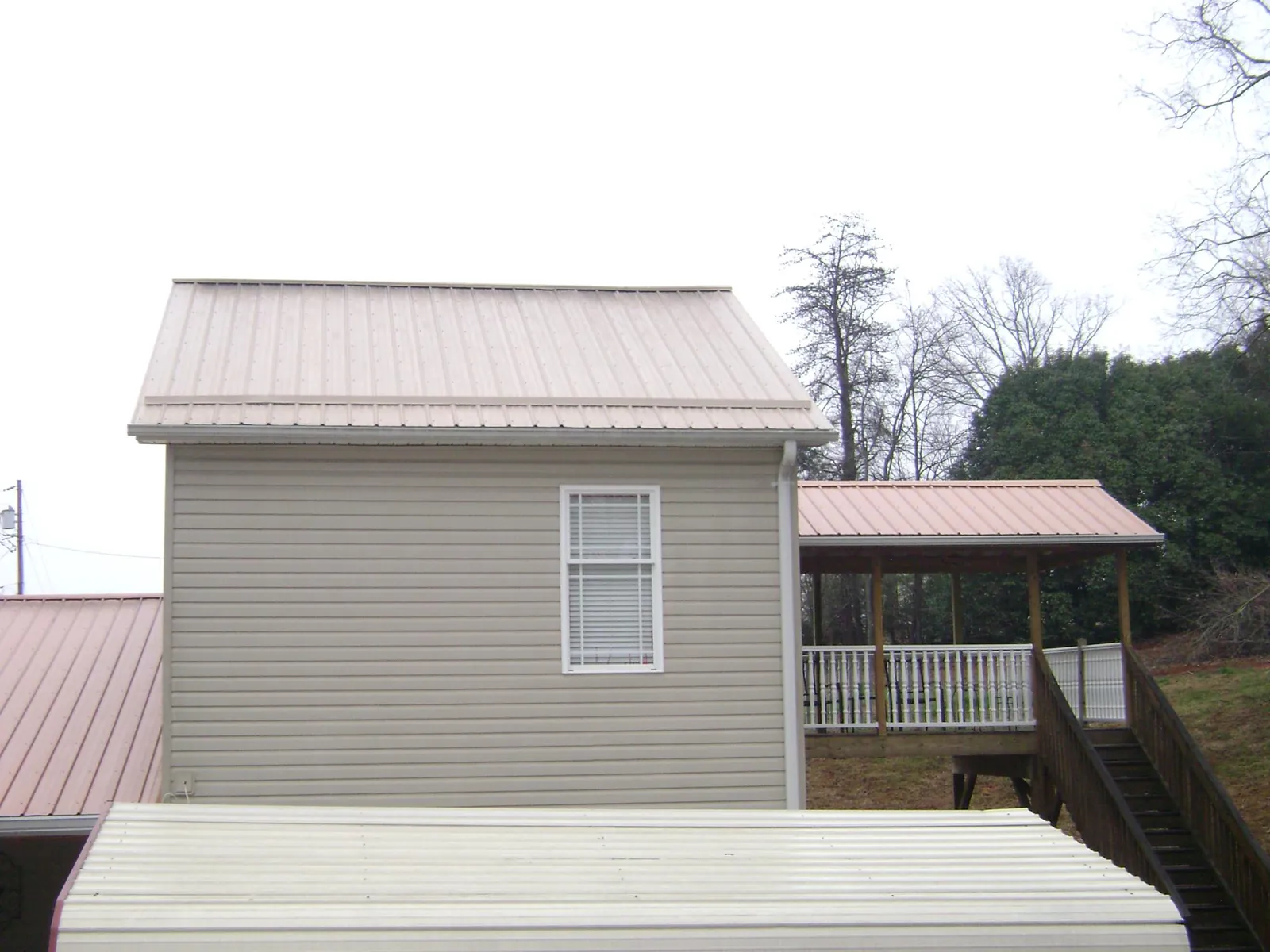 Tan metal roofs on a two story addition and attached porch, from a Roof Replacement job in Beatrice